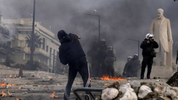 A protestor throws a stone against the riots police outside of the parliament during a rally in central Athens, Greece, on Friday, Feb. 28, 2025