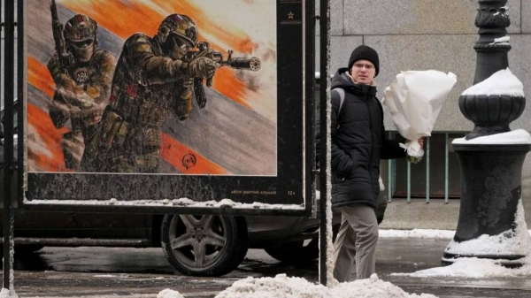 A man carries a bouquet of flowers walking past a street exhibition of military posters dedicated to Russian army during Valentine's Day in St Petersburg, 14 February 2025