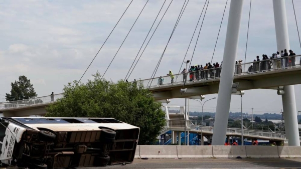 Pedestrians standing on a bridge look at a bus that overturned on a highway in Johannesburg, South Africa, on 11 March, 2025