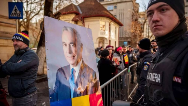 A portrait of Calin Georgescu, is placed on a crowd control fence by supporters waiting for his arrival at a district