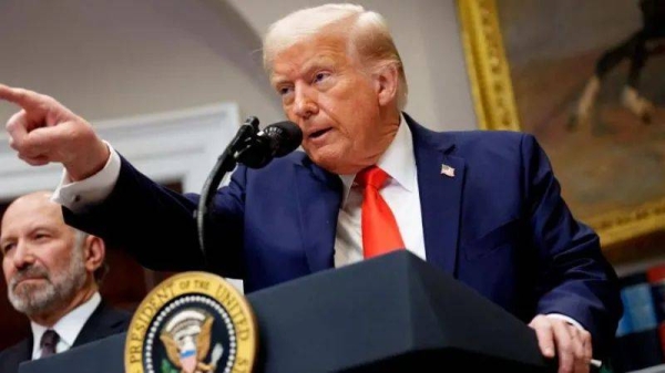 US President Donald Trump, wearing a blue suit and orange tie, pointing at an audience member while he speaks at a lectern