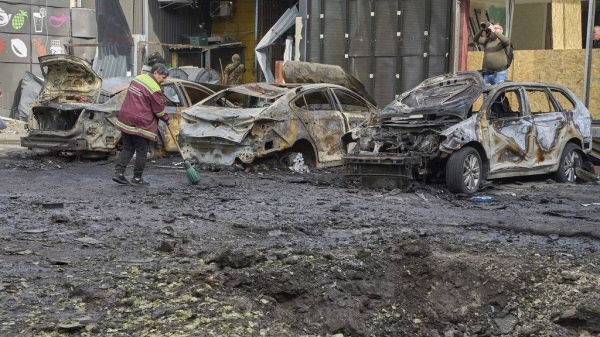 Municipal workers clean up near burnt cars and a crater made by a drone in the residential area following Russia's air raid in Kyiv, Ukraine, Sunday, May 4, 2025