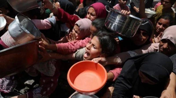 A large group of Palestinians wait to receive food cooked by a charity kitchen, in Jabalia, in the northern Gaza Strip.  They are holding on pans and other receptacles and look distressed