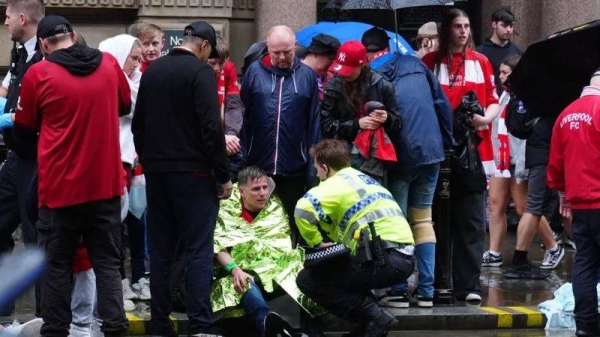 A police officer crouched down talking to man wrapped in emergency service blanket at he sits on the floor