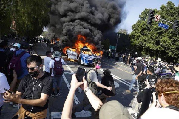 People watch while several Waymo cars burn in Los Angeles after being vandalized by protesters reacting to a series of immigration raids, on Sunday, June 8, 2025