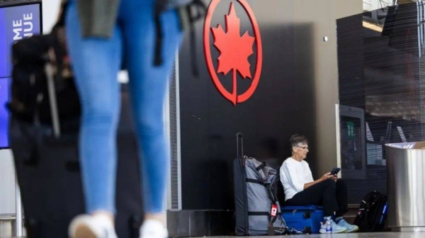 A middle-aged male passenger waits with his luggage at Toronto Pearson Airport while a woman in jeans can be seen in the foreground pulling a suitcase