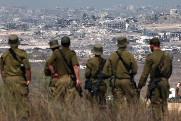 Israeli army soldiers look at destroyed buildings in the Gaza Strip as they stand on the border with the Palestinian territory on Wednesday