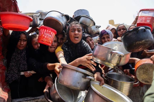Palestinians gather to receive cooked meals from a food distribution center in Gaza City on August 13, 2025