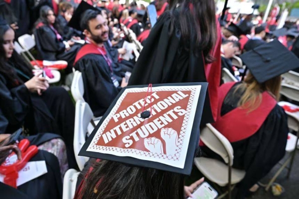 A Harvard University graduate with a message in support of international students on her mortarboard sits with fellow students at the start of commencement exercises at Harvard University in Harvard Yard May 29, 2025,