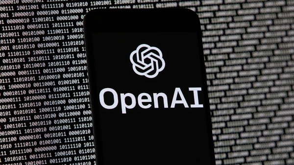 The OpenAI logo appears on a mobile phone in front of a computer screen with random binary data, March 9, 2023, in Boston