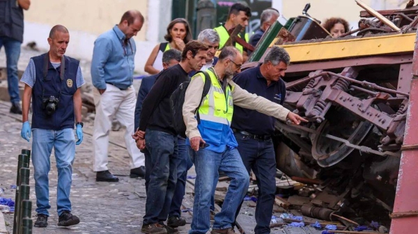 Several men inspect the mangled metal of a crashed train carriage.
