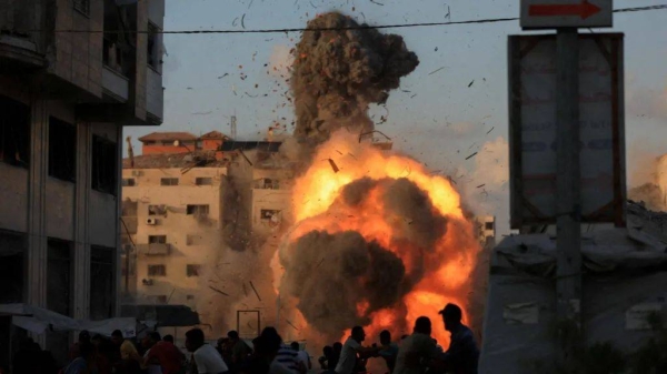 A large explosion of fire and smoke can be seen, after a strike on a building in Gaza. People can be seen running from the explosion, and rubble is flying through the air