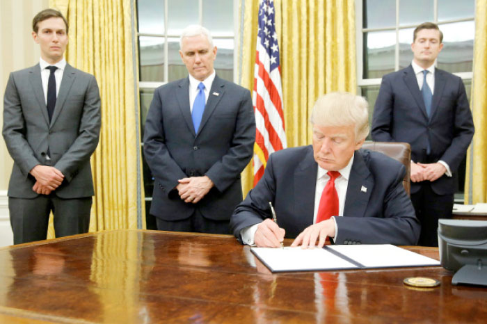 US President Donald Trump, flanked by Senior Adviser Jared Kushner (standing, L-R), Vice President Mike Pence and Staff Secretary Rob Porter, signs his first executive orders at the White House in Washington. — Reuters
