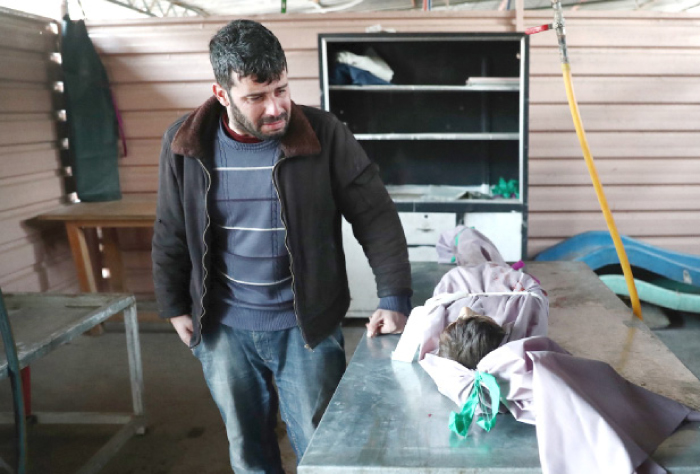 A father mourns over the body of his 11-year-old son, Ahmad, who was reportedly killed along with a friend when a cluster bomb exploded in his backyard, at a makeshift morgue in the rebel-held town of Douma, on the eastern outskirts of the capital Damascus, on Friday. — AFP