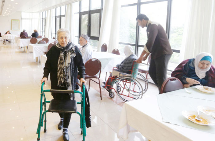 Syrian Lamis Al-Haffar (left), 82-year-old general manager of Dar Al-Saada retirement home, moves with the help of a walker at the home, in the Syrian capital Damascus. Residents at the home pay a monthly fee of $120 for meals, care and a bed in a room with two other people, equipped with a television, a small table and an electric heater. — AFP