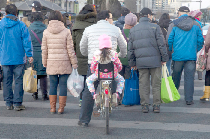 A child rides behind a man as they cross the road by bicycle in Beijing, China, on Sunday. — AP