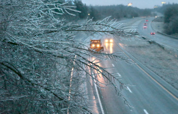 A Missouri Department of Transportation salt truck spreads ice melt on Interstate 55 as coated tree branches sway overhead as seen from the Main Street bridge in Festus, Missouri, on Friday. — AP