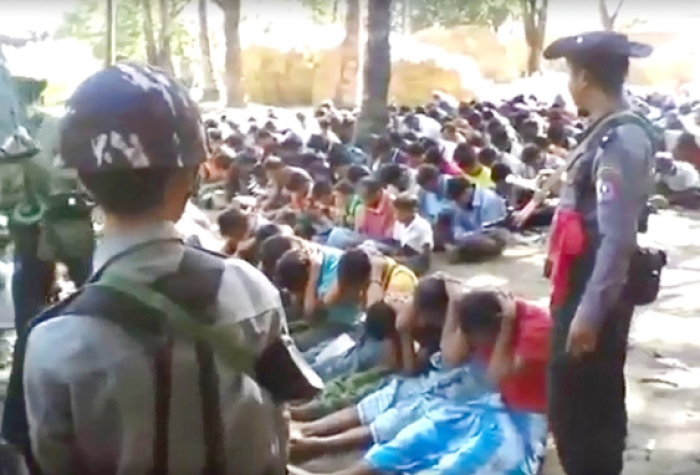 This screen grab taken on Wednesday from a YouTube video originally taken by Myanmar Constable Zaw Myo Htike, not pictured shows policemen standing guard around Rohingya minority villager seated on the ground in the village of Kotankauk during a police area clearance operation on Nov. 5, 2016. — AFP