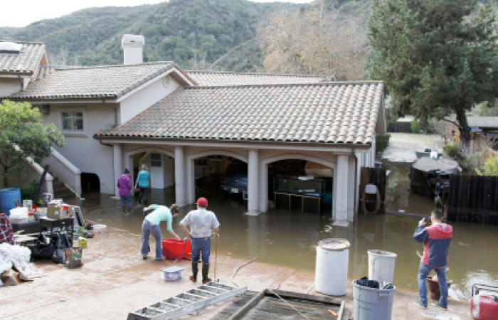 People at a home in Carmel Valley, Calif., work to recover water-damaged items from a downstairs living area and garage on Monday, after heavy rains caused the nearby Carmel River to overflow Sunday. — AP