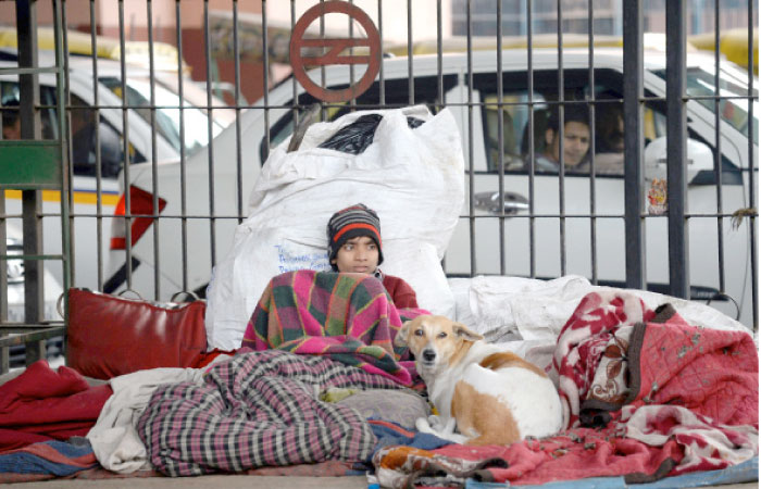 An Indian homeless man wrapped in a blanket sits on a footpath during a cold morning in New Delhi on Tuesday. — AFP
