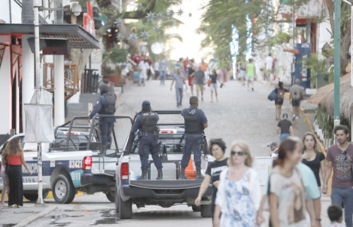 Municipal police trucks drive past strolling tourists, as they leave the Blue Parrot club, where several people were killed in early morning gunfire, in Playa del Carmen, Mexico, on Monday. — AP