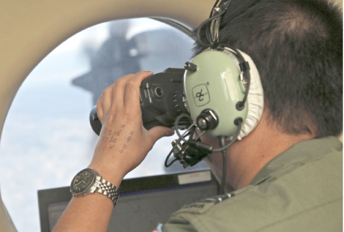 Flight Officer Jack Chen uses binoculars at an observers window on a Royal Australian Air Force P-3 Orion during the search for missing Malaysia Airlines Flight MH370 in Southern Indian Ocean, Australia, in this March 22, 2014 file photo. — AP