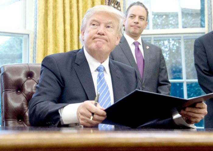 US President Donald Trump signs an executive order as Chief of Staff Reince Priebus looks on in the Oval Office of the White House in Washington, D.C. on Monday. — AFP