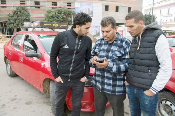 Moroccan taxi drivers check the Uber app as they wait for customers in Casablanca. — AFP