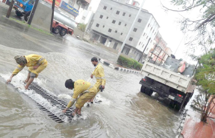 Asir Municipality workers clearing a clogged drain to release water from a flooded street. — SPA