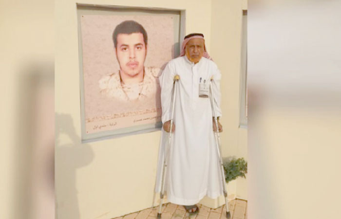 Hadi Hassan Assiri, who lost his right leg during the Gulf War, stands near the portrait of his son who was martyred defending the homeland in Jazan last year. — Courtesy: Al Arabiya