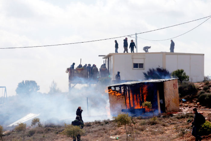 Protesters stand atop a roof and balcony as a shed burns during an eviction by Israeli police of residents from the Israeli settler outpost of Amona in the occupied West Bank on Wednesday. — Reuters