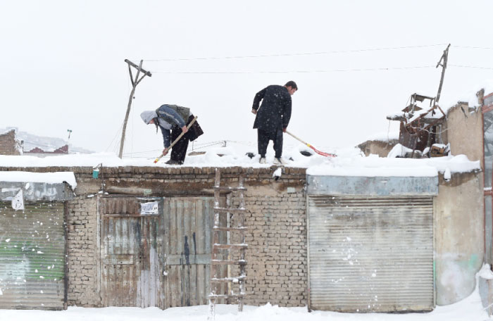 Afghan shopkeepers shovel snow from the roof of their shop during snowfall in Kabul on Sunday. — AFP