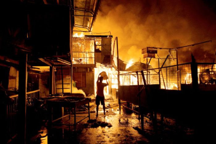 A resident pours water on a fire as it destroys hundreds of  houses at an informal settlers community in Delpan, Tondo, Manila on Tuesday. — AFP