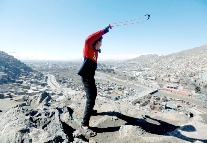 An Afghan boy plays with a sling outside his house at a hill top in Kabul, Afghanistan, on Monday. — Reuters