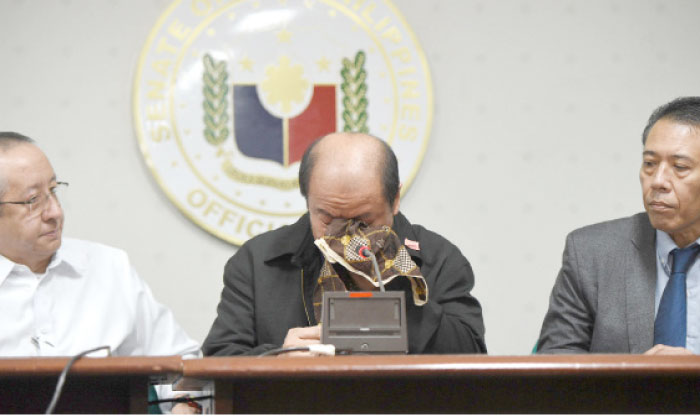 Former police officer Arthur Lascanas, center, wipes his tears as he relates the death of his brothers, during a press conference next to lawyers from the Free Legal Assistance group Arno Sanida, left, and Manuel Diokno III, right, at the Senate in Manila on Monday. — AFP