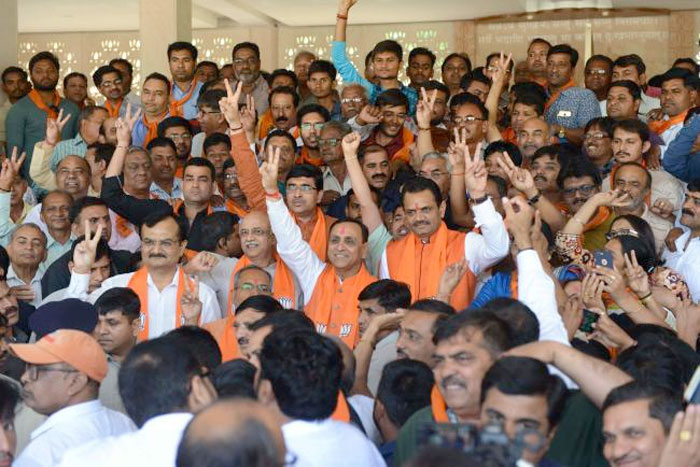 Gujarat state Chief Minister, Vijaybhai Rupani (C), Gujarat state Bhartiya Janta Party (BJP) President, Jitubhai Vaghani (CR) with other dignitaries and BJP supporters show victory signs as they assemble at 'Kamalam', Koba near Gandhinagar, some 20 kms from Ahmedabad. — AFP