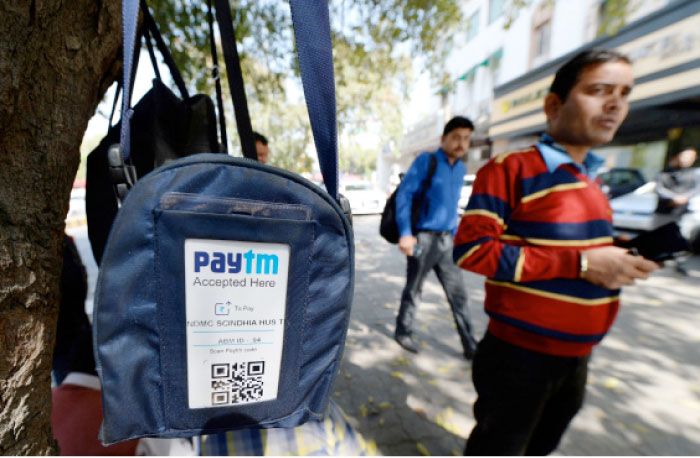 An Indian car park attendant stands beside a bag with a logo advertising Indian electronic and cellphone-based payment system Paytm outside a parking area in New Delhi. — AFP