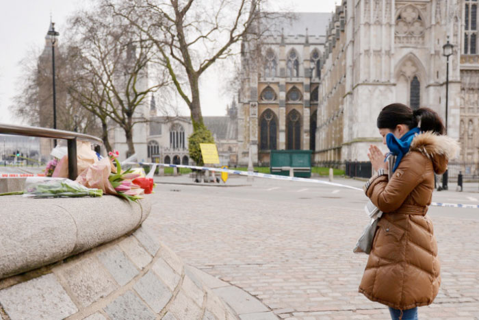 A woman pays her respects facing a floral tribute close to the Houses of Parliament in central London on Thursday following the Wednesday terror attack in Westminster. — AFP