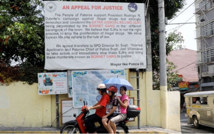 A motorist drives a motorcycle past a banner denouncing the Bonnet Gang, a group allegedly involved in drug related killings in the town of Pateros, Metro Manila. — Reuters photos