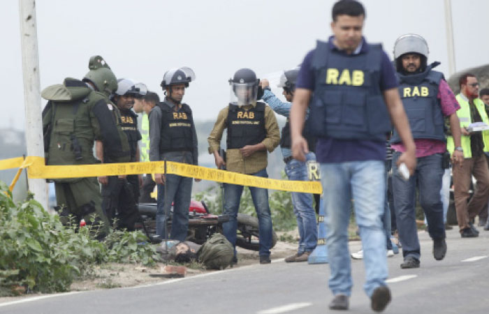 Bangladesh Rapid Action Battalion (RAB) personnel and bomb experts stand near the body of a man beside a RAB checkpoint in Khilgaon, Dhaka, Bangladesh, on Saturday. — AP