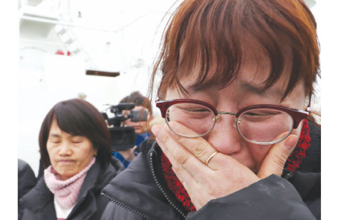 Relatives of the missing from the Sewol ferry disaster cry as they watch as a part of the damaged Sewol ferry is raised between two barges during a salvage operation at sea off the southwestern island of Jindo on Thursday. — AFP