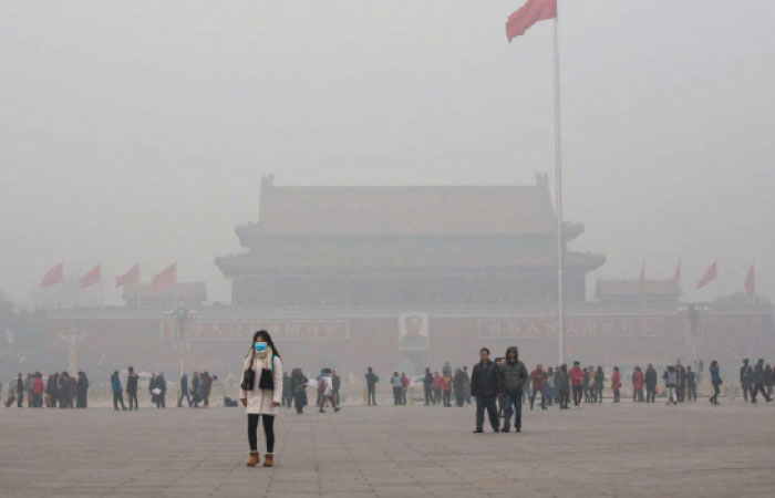 A Chinese woman protects herself with a mask as she walks past Tiananmen Square in smog. — File photo