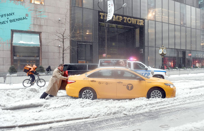 A passenger pushes a cab stuck on a snow and sleet-covered street in New York on Tuesday. — AFP