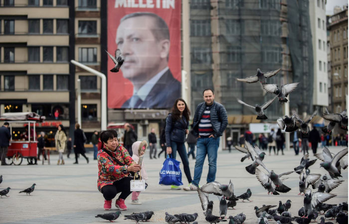 A woman feed pigeons next to a poster of Turkish President Recep Tayyip Erdogan in Istanbul. — AFP