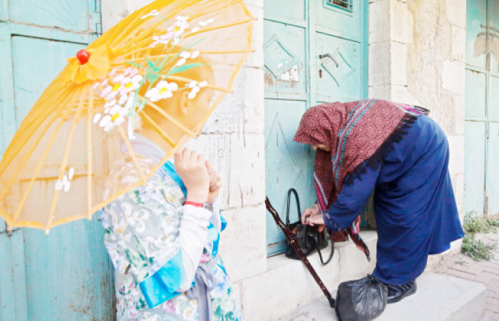 An Israeli settler (L) wearing a costume looks at a Palestinian woman standing in front of her house during a parade to celebrate the Jewish holiday of Purim in Al-Shuhada Street, in the West Bank town of Hebron. — AFP