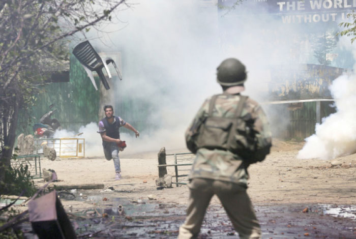 A Kashmiri student throws a chair on Indian policemen as they clash in Srinagar, Indian controlled Kashmir, on Monday. — AP