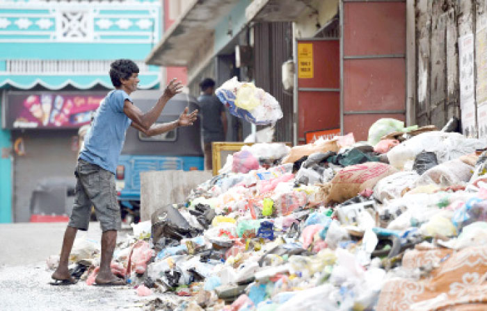 A Sri Lankan man throws garbage onto a rubbish pile on a street in Colombo on Tuesday. — AFP