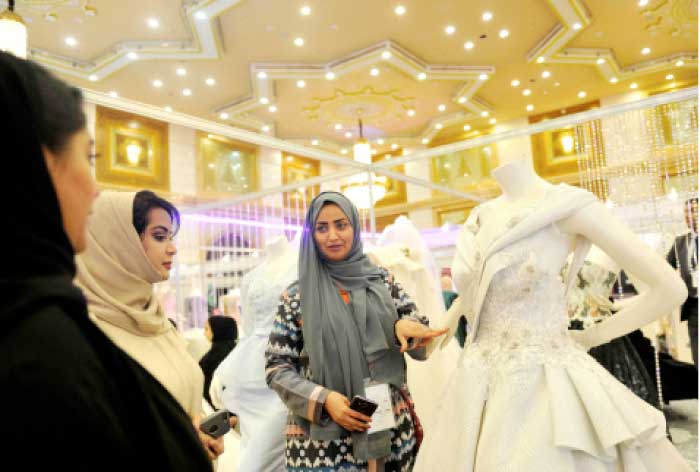 A Saudi woman shows wedding dresses to women at a bridal expo in Jeddah. — AFP