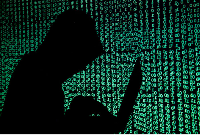 A hooded man holds a laptop computer as cyber code is projected on him in this illustration picture taken. — Reuters