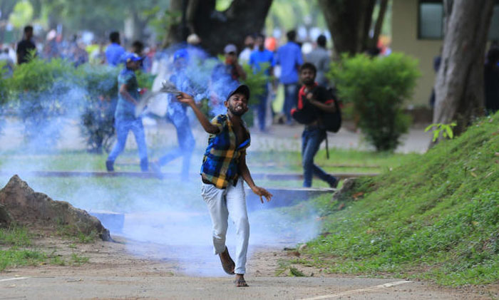 A Sri Lankan university student throws back a tear gas canister fired by police to disperse them during protest in Colombo on Wednesday. — AP